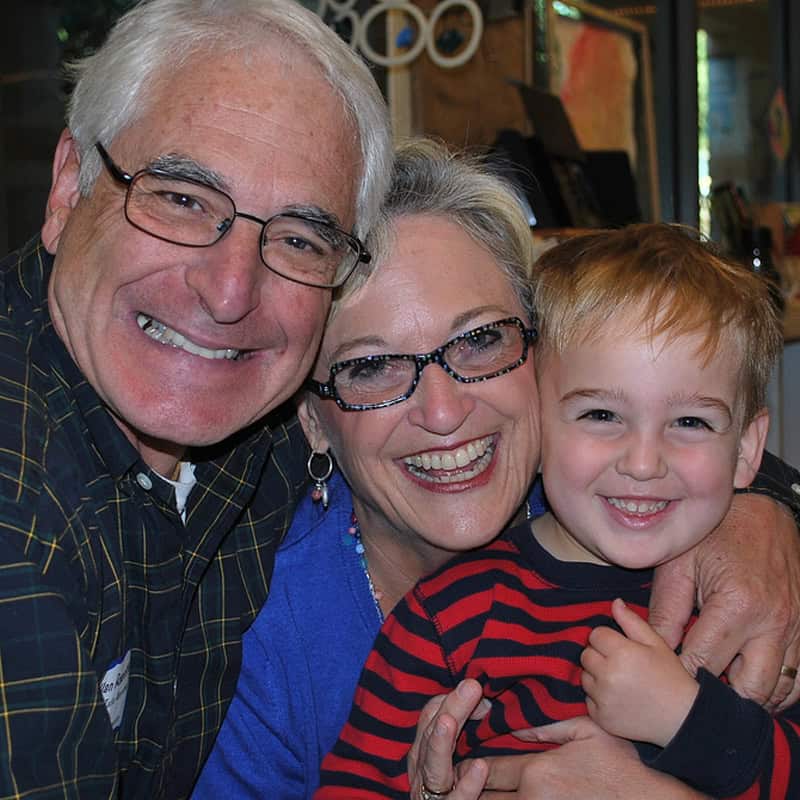 A grandmother and grandfather smile and hug their young grandson.