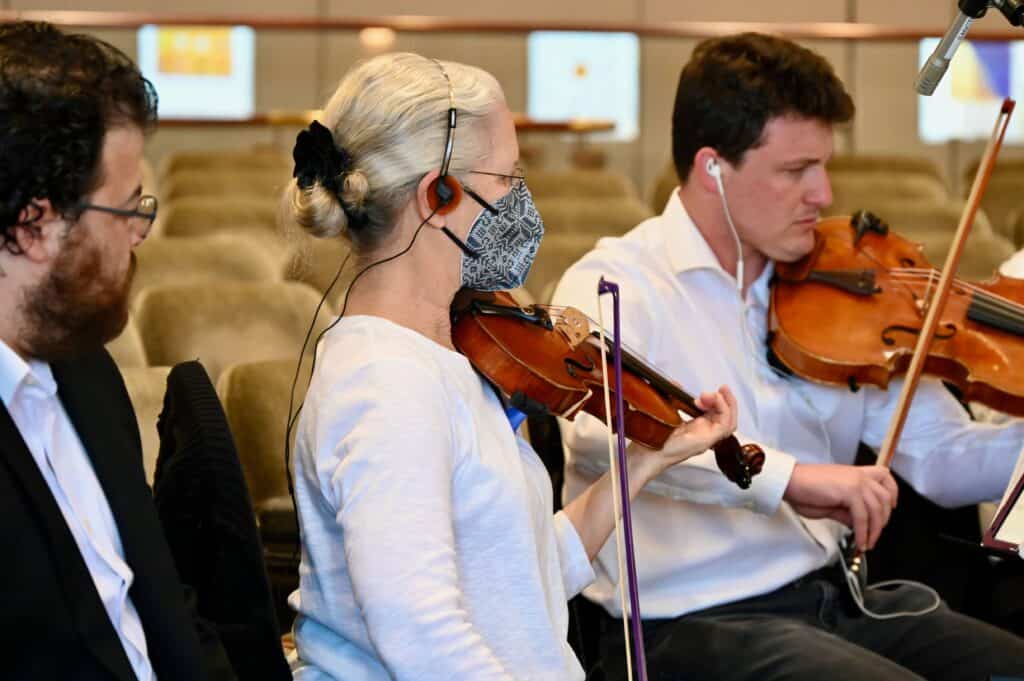 A woman and a man each play the violin during CBI's Contemporary Yizkor Service.
