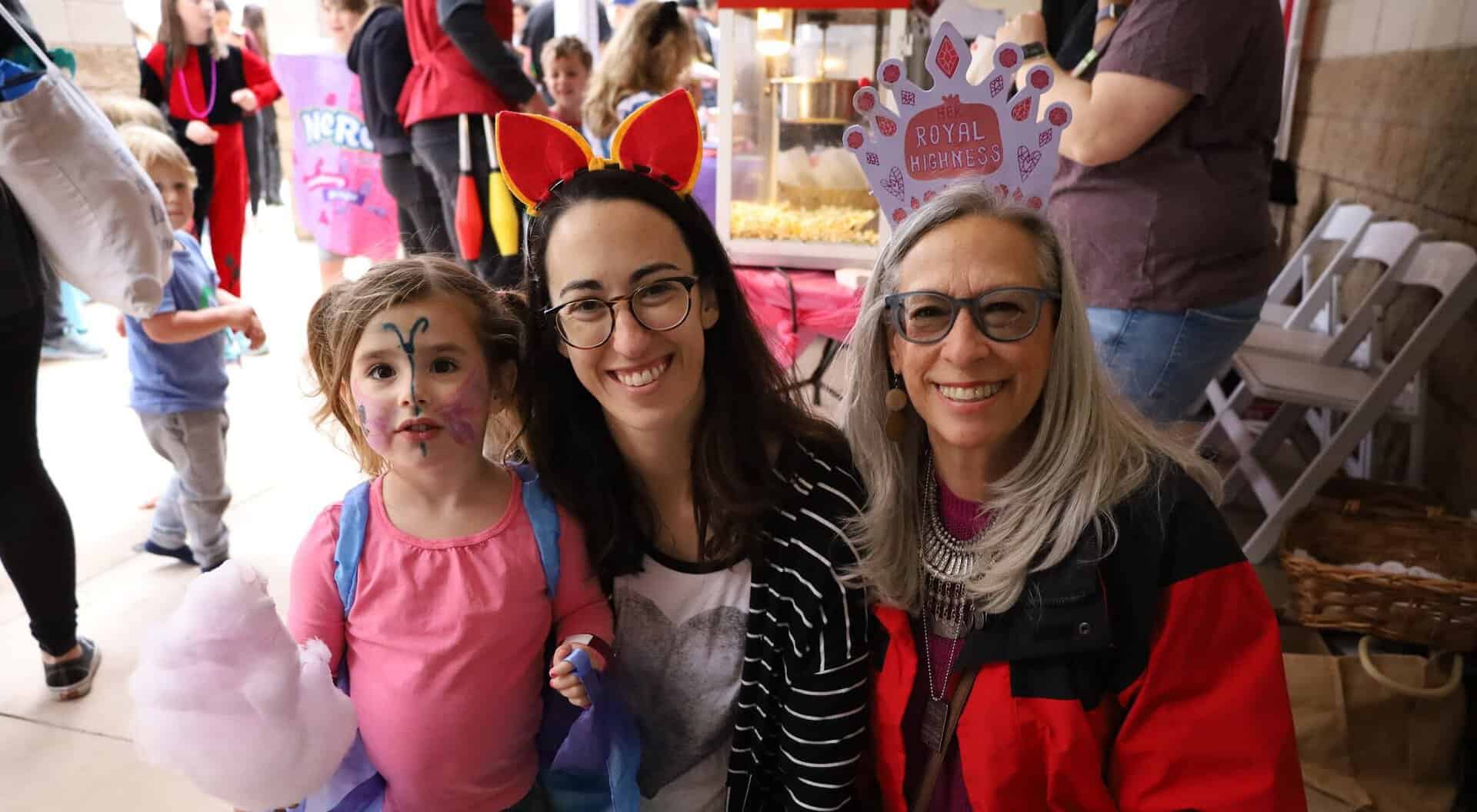 Two women and a young child smile and pose during the CBI Purim Carnival