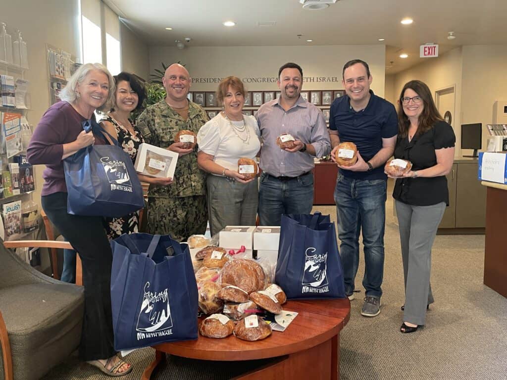 Group of people posing with baked challah as part of a Caring Community event