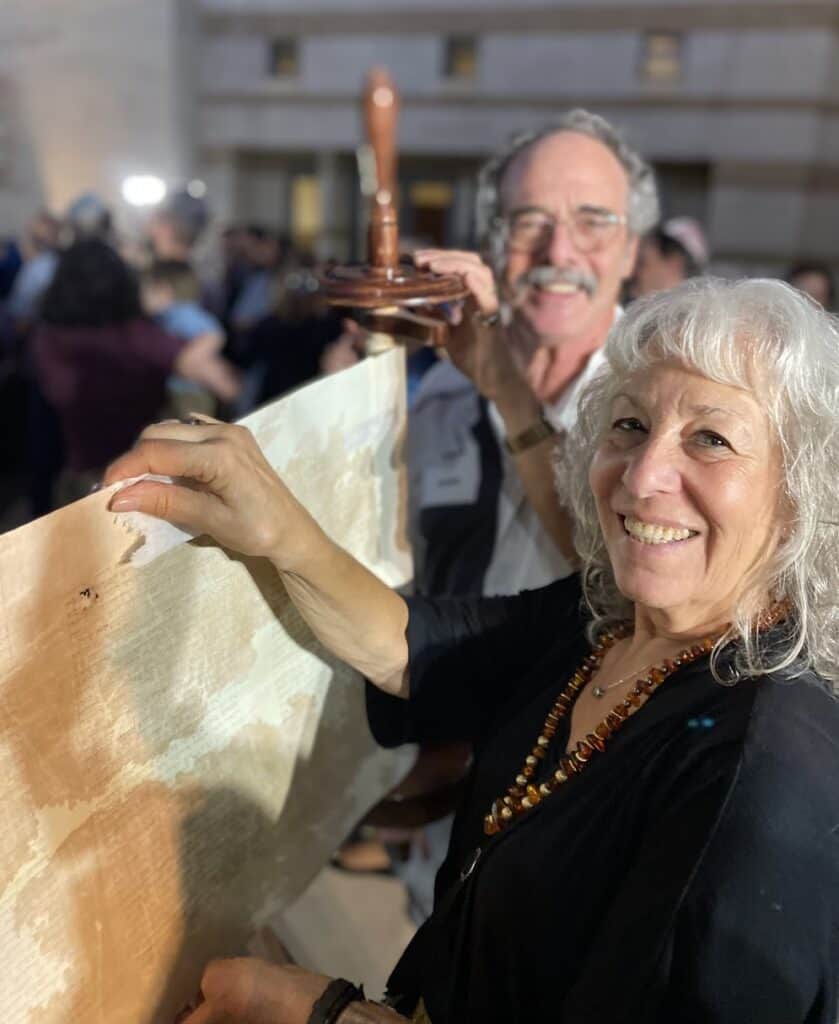 A man and a woman hold up an unrolled Torah scroll during the Simchat Torah celebration.