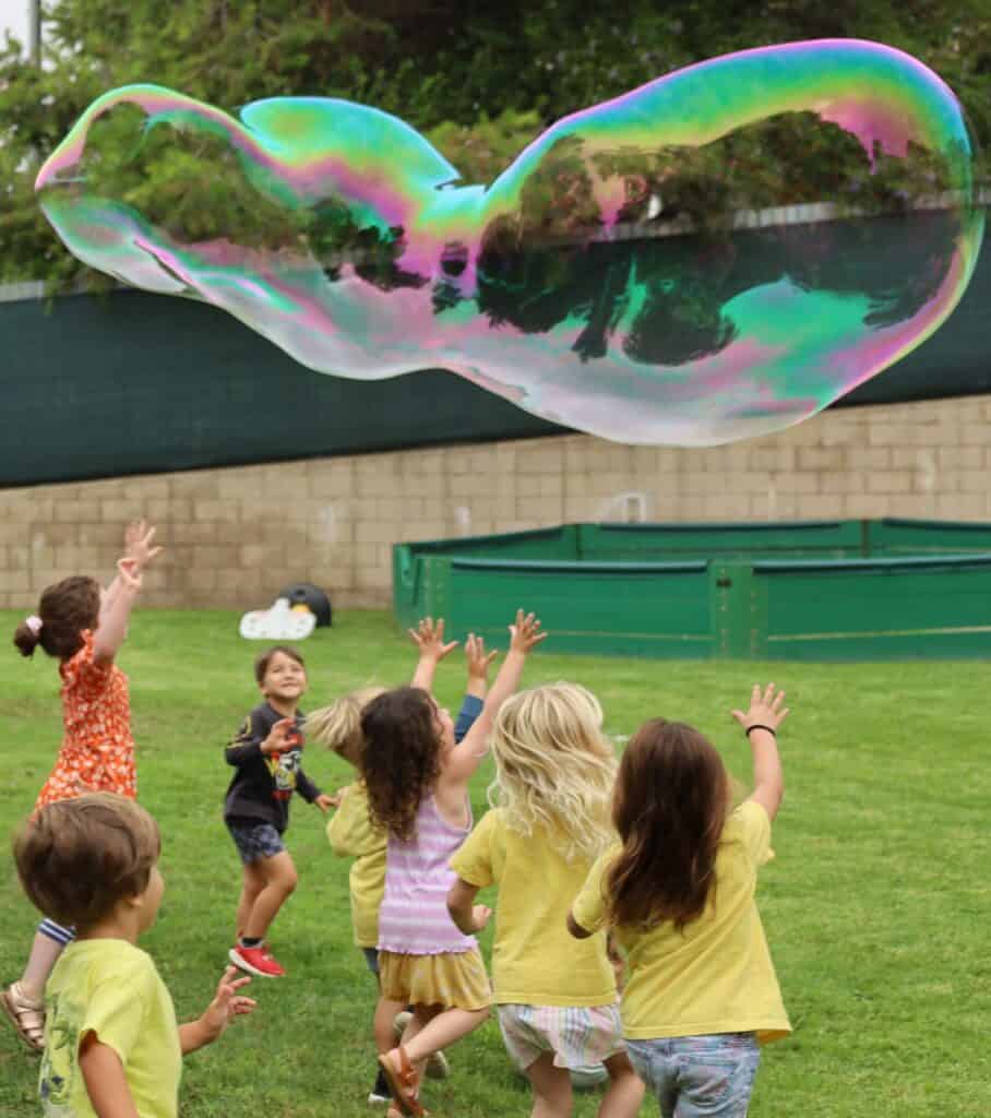 Children chase an extra large bubble as it floats through the air.