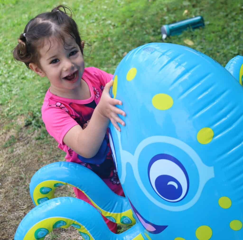 A small child laughs while playing with an inflatable octopus.