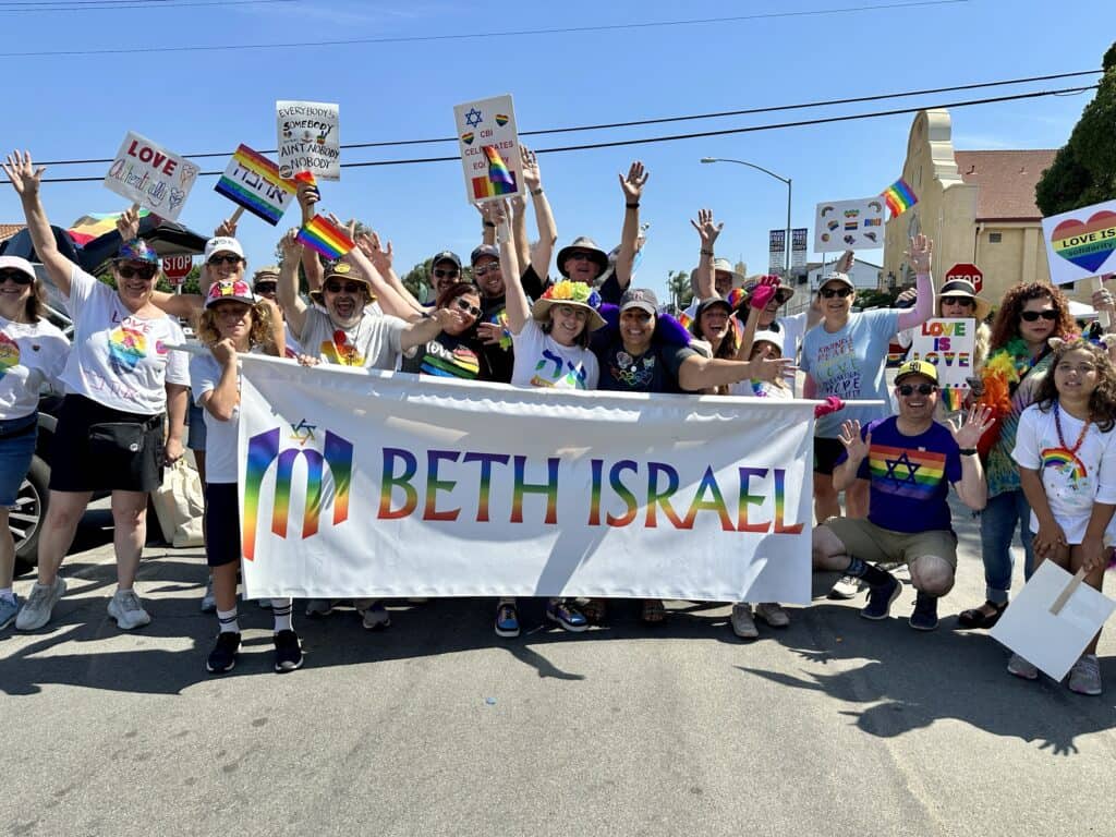 Group of people in rainbow clothing holding a rainbow Beth Israel sign at a parade