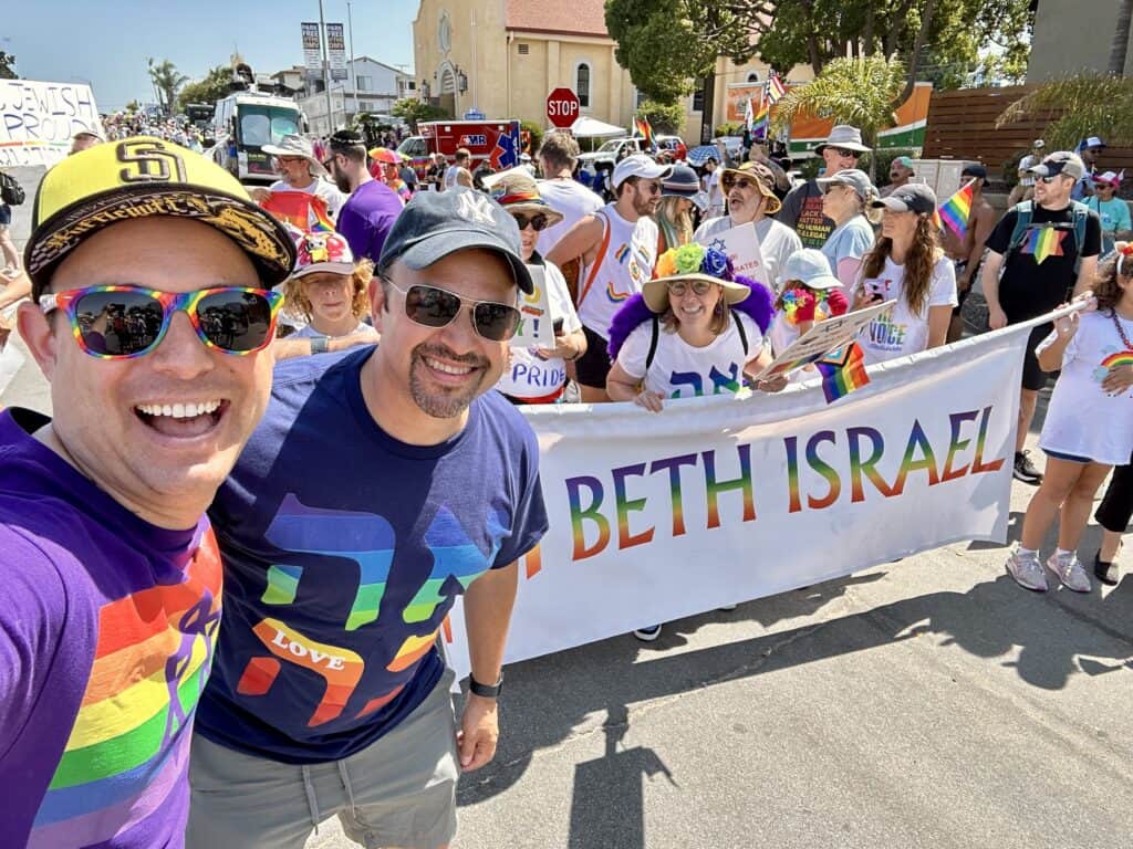 Group of people in rainbow clothing posing with a rainbow Beth Israel sign at a parade