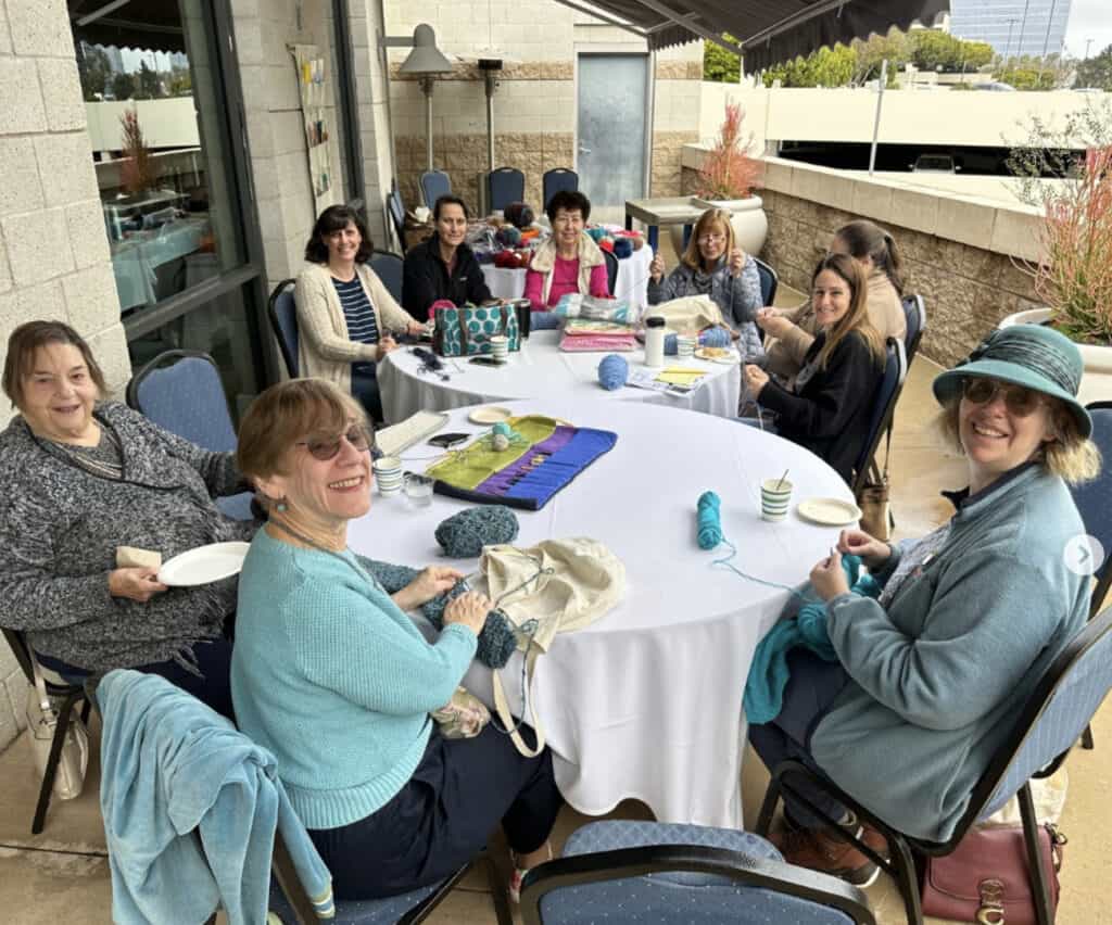 CBI members sit together at a table during a member meet up knitting event.