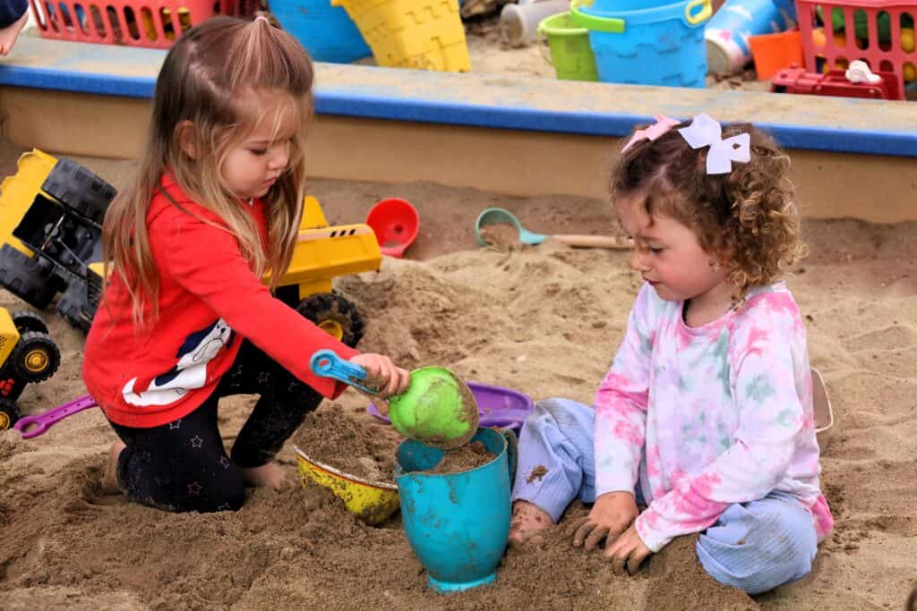 Two preschool students playing in the sandbox together.