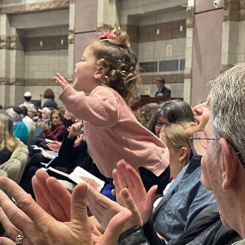 A young toddler dances on her parent's lap during services
