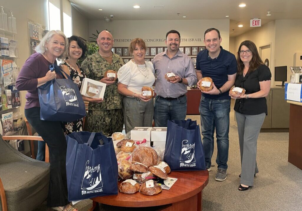 Group of people posing with baked challah as part of a Caring Community event