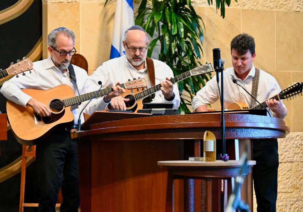 Three men stand on the Bimah, playing guitar during the Contemporary Yizkor Service.