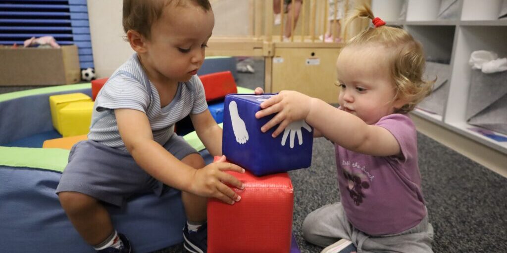 Two infants build with plush blocks inside of a classroom