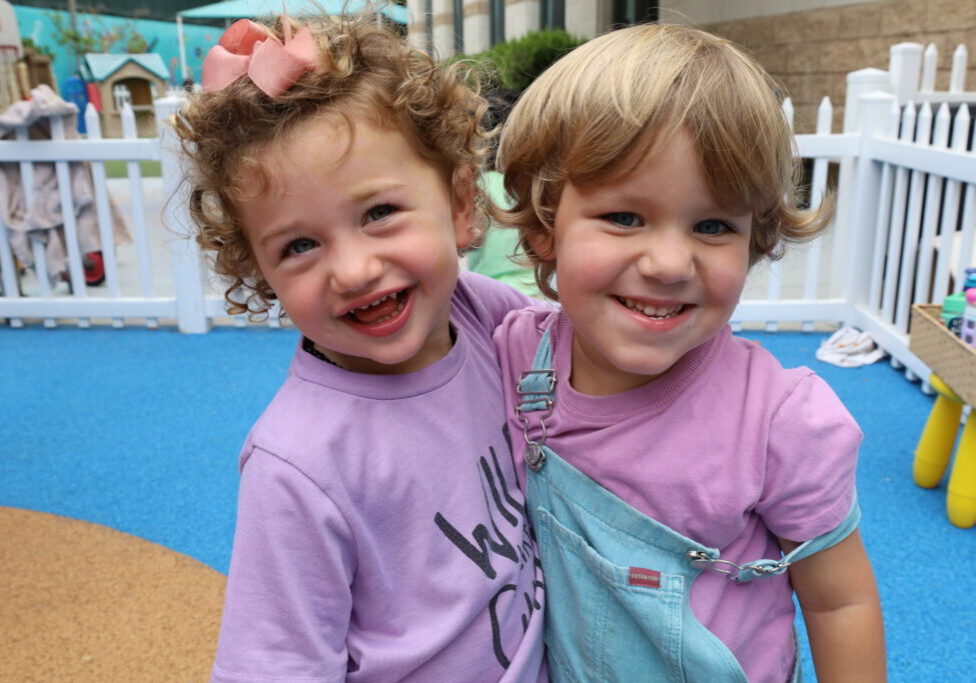 Two young preschoolers smile on the playground