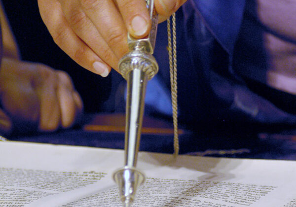 A close up of a hand using a pointer to aid in reading from the Torah.